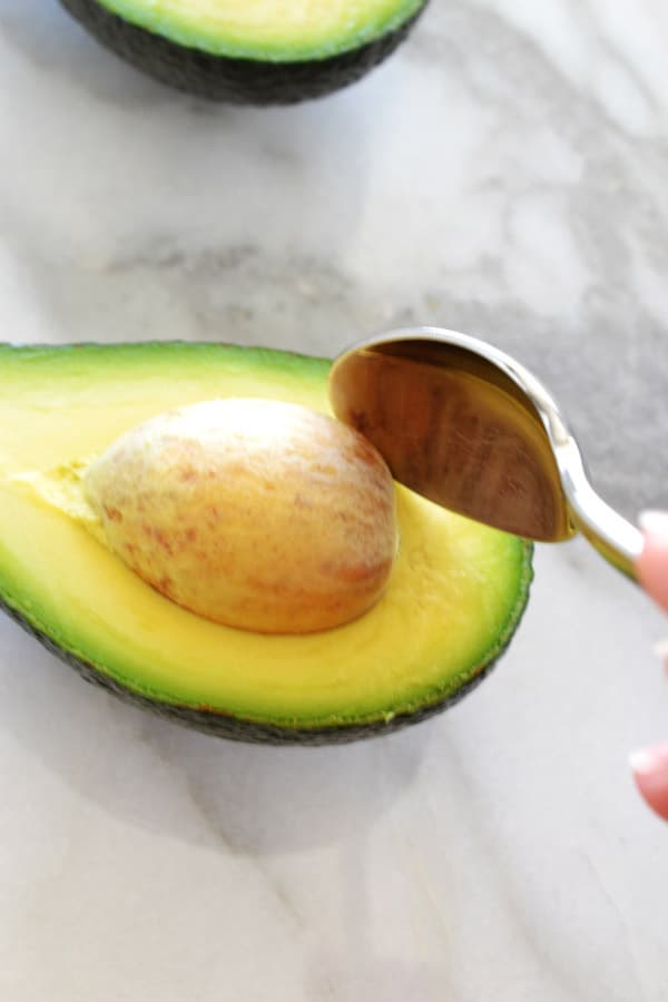 half and avocado with spoon removing pit