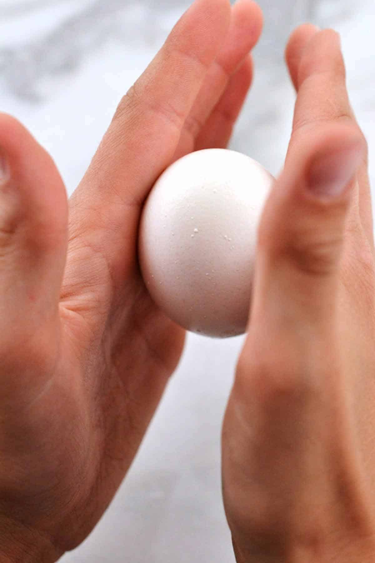 Rolling a cracked hard-boiled egg between palms to loosen shell.