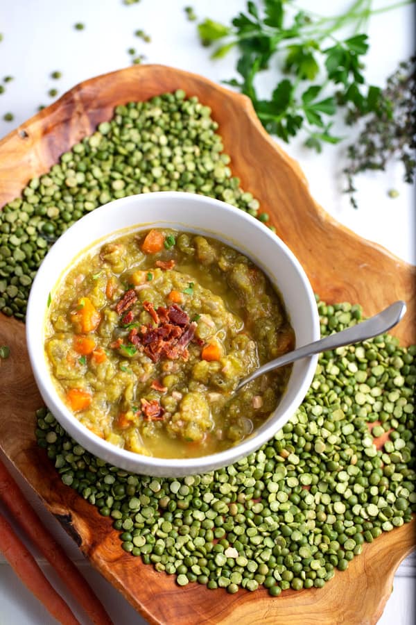 bowl of split pea soup surrounded by dry split peas and fresh herbs