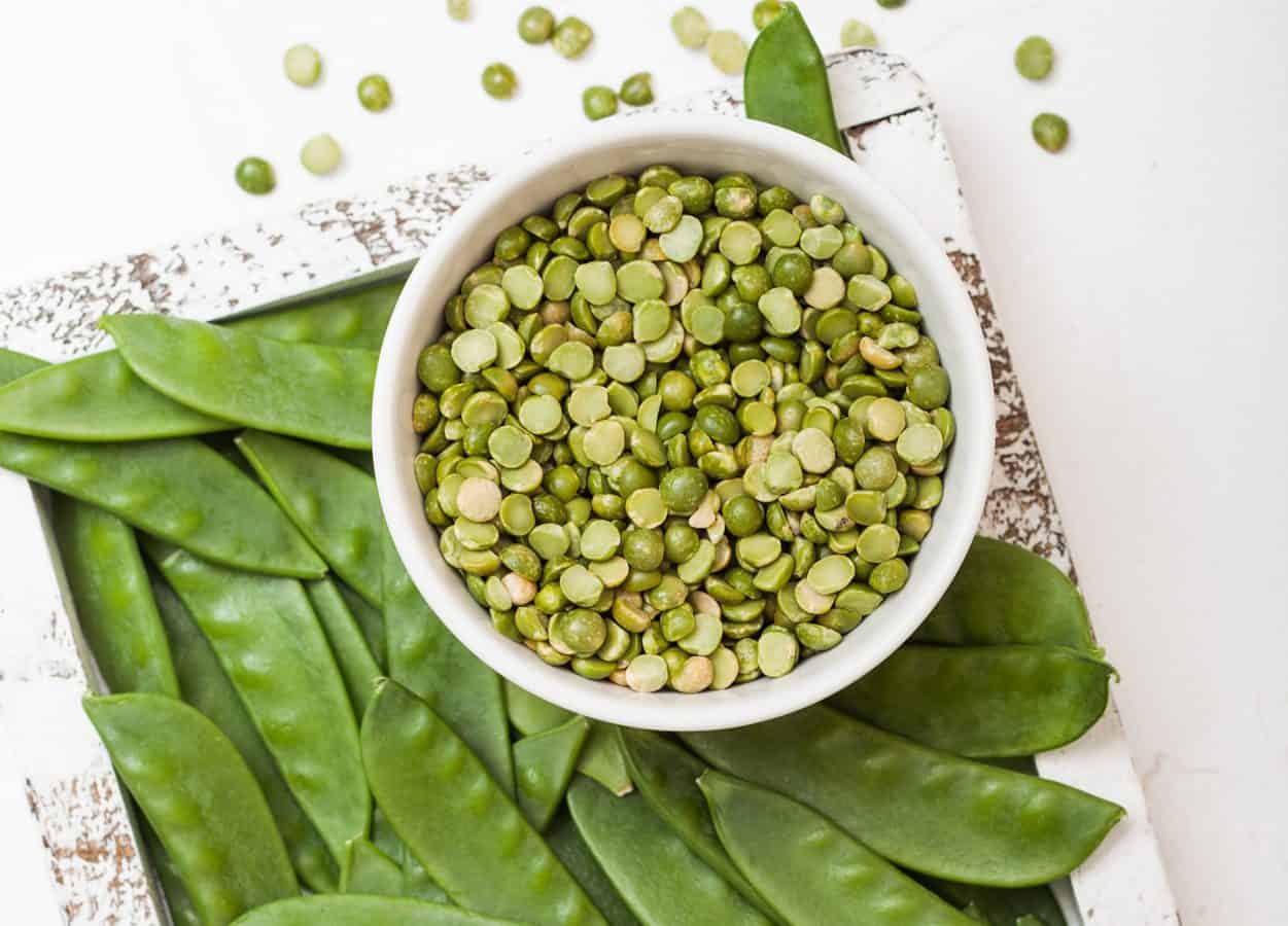 bowl of split peas surrounded by pea pods