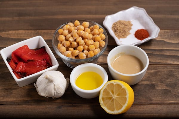 bowls of ingredients for roasted red pepper hummus (red peppers, chickpeas, garlic, lemon, olive oil, tahini, and spices)