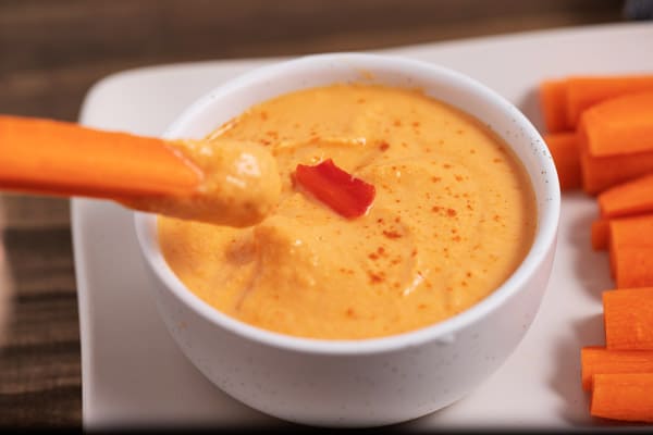 dipping a carrot stick in a bowl of roasted red pepper hummus