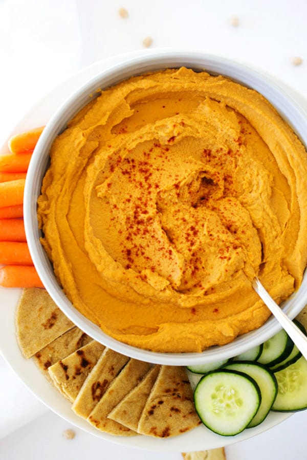 bowl of hummus surrounded by carrots, cucumbers, and pita bread