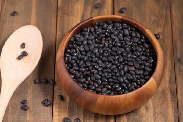 bowl of raw black beans and wooden spoon