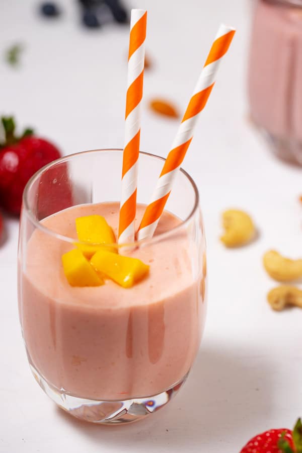mango strawberry banana smoothie in a glass with two straws