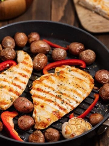 cooked chicken breast in grill pan with potatoes and red peppers
