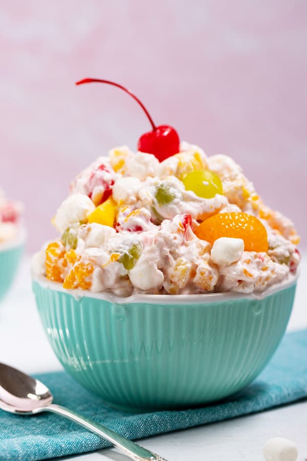 bowl of ambrosia salad with a cherry on top and a spoon on the side