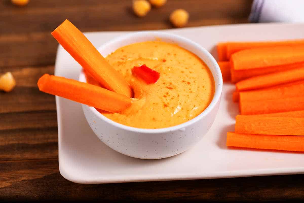 Bowl of roasted red pepper hummus with carrots.