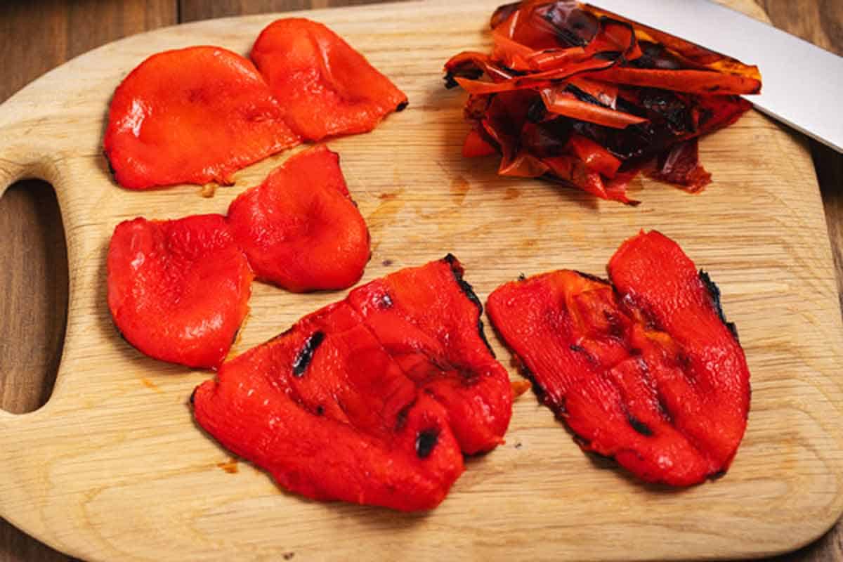 Red pepper skins in a pile next to the peeled peppers.