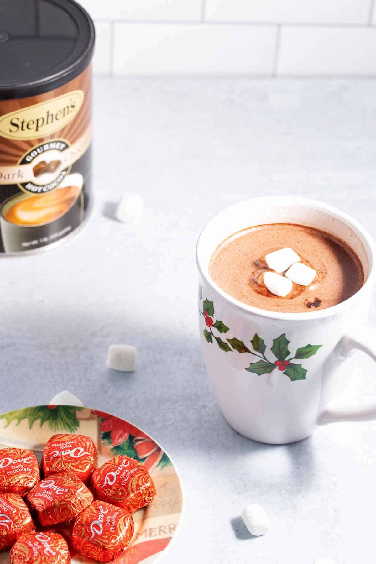 Hot chocolate with marshmallows next to a plate of chocolate candies.