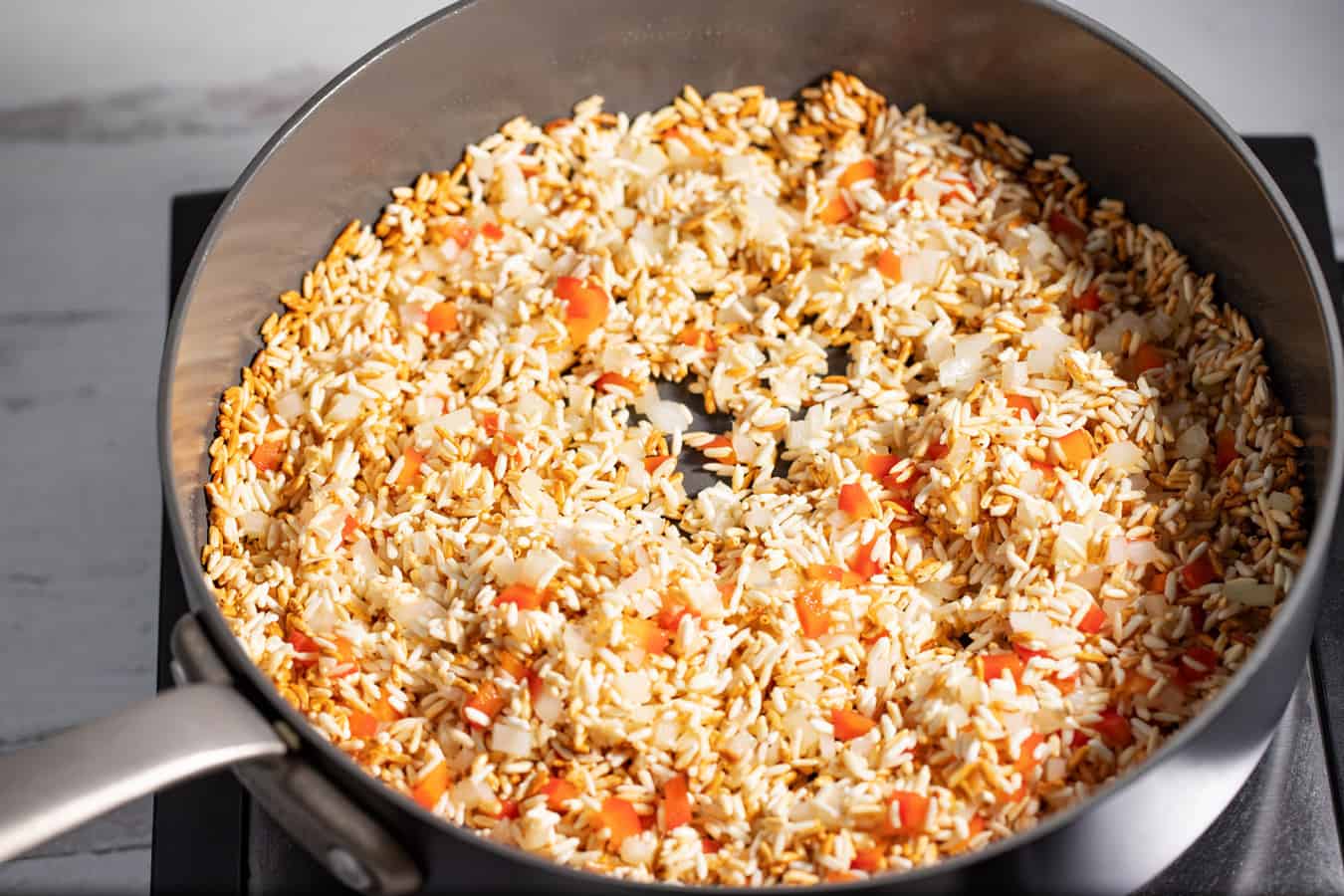 toasted rice with diced onion and red pepper in skillet