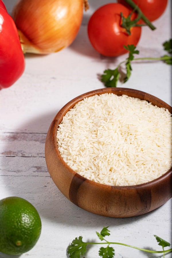 bowl of raw white rice surrounded by lime, cilantro, tomatoes, onion, and red bell pepper