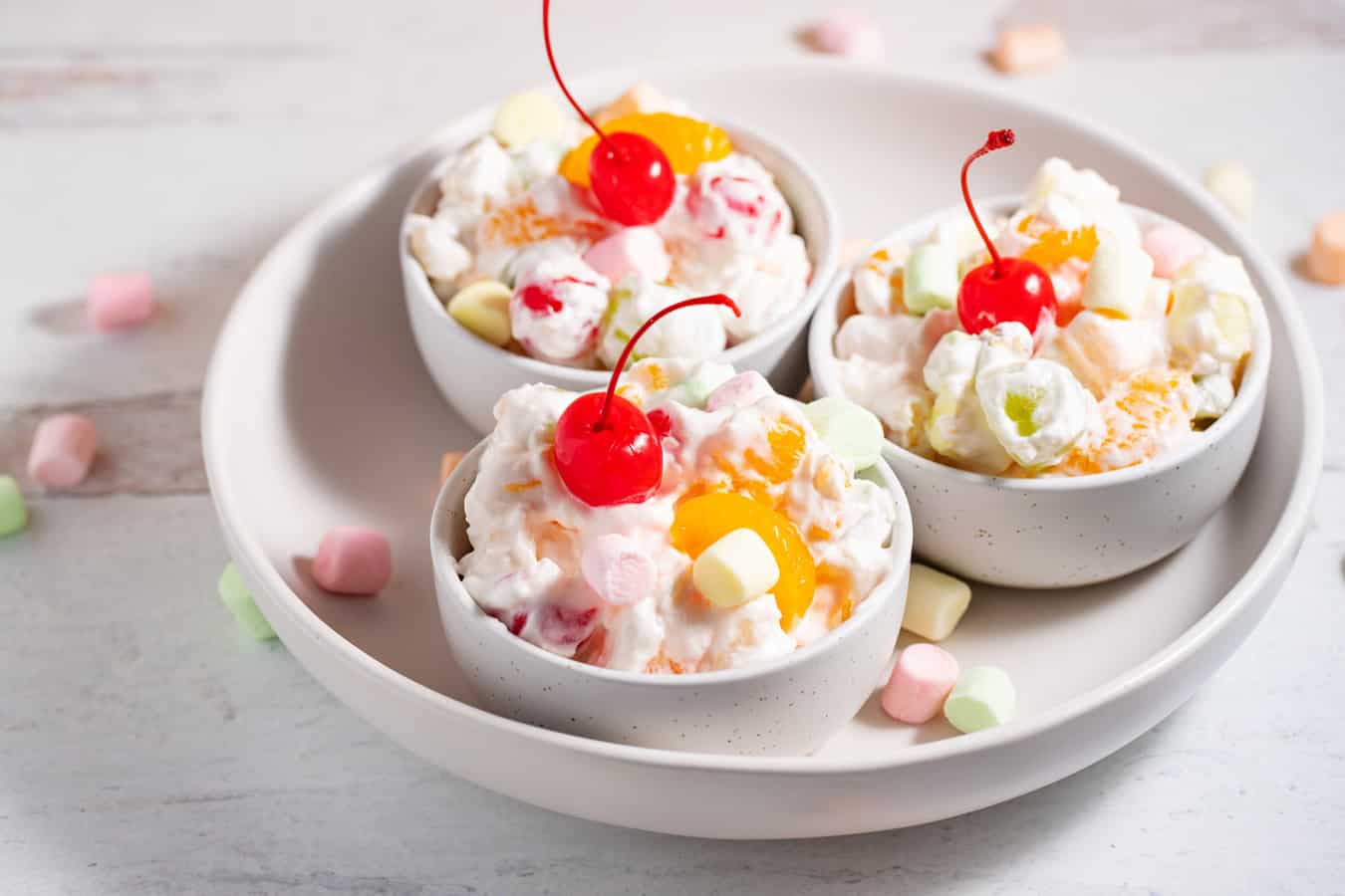 3 serving bowls of ambrosia salad with a cherry on top