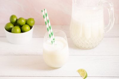 glass of Brazilian lemonade next to a pitcher and a bowl of key limes