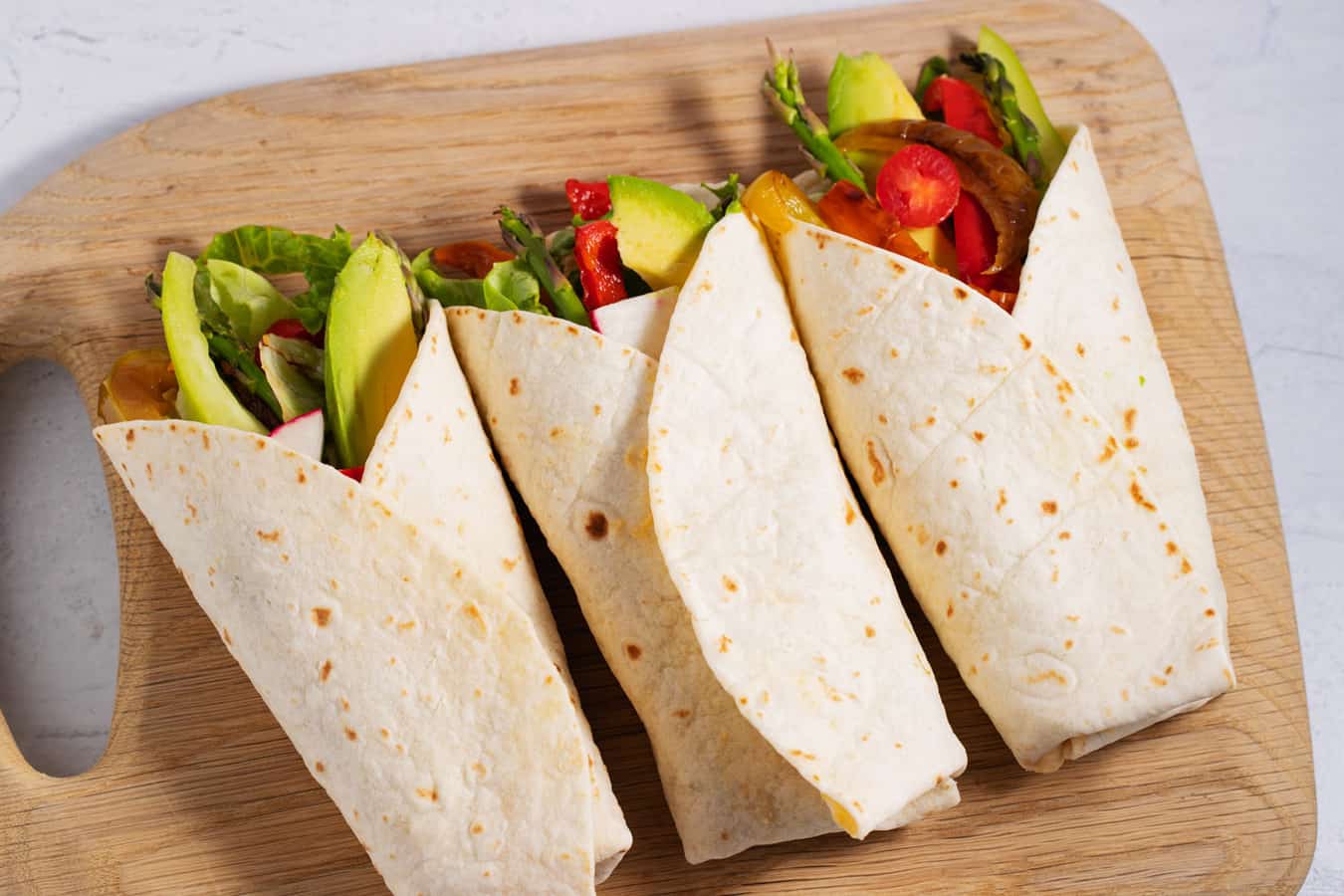 3 veggies wraps on a cutting board.