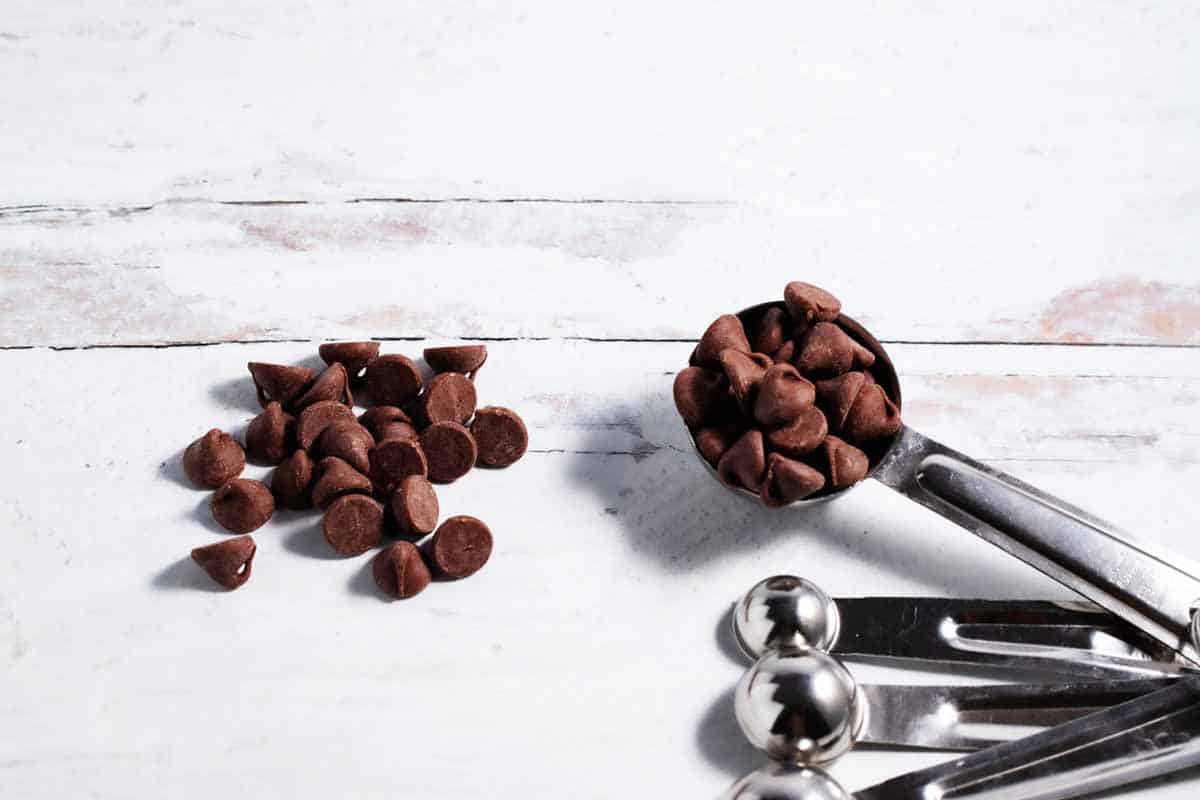 A tablespoon with chocolate chips next to a pile of chocolate chips.