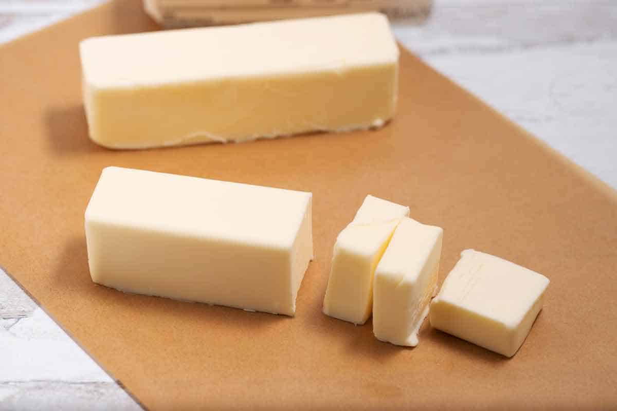 Two cubes of butter with 3 butter pats cut on parchment paper.