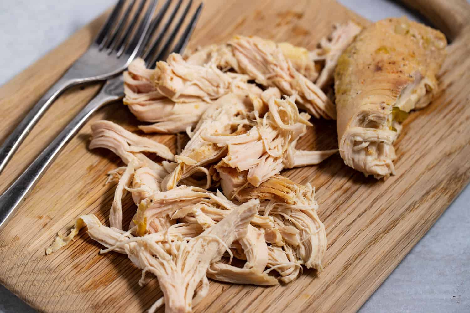 shredded chicken on a cutting board with two forks