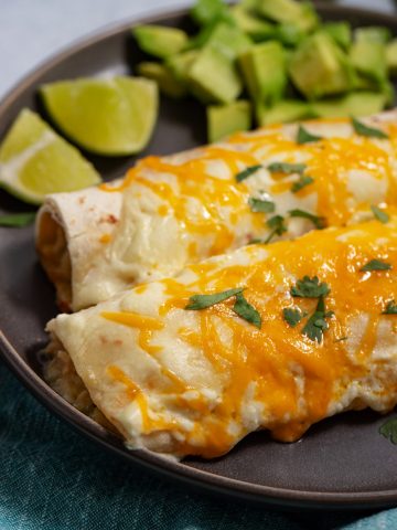 2 chicken enchiladas on a plate with lime wedges and avocado cubes