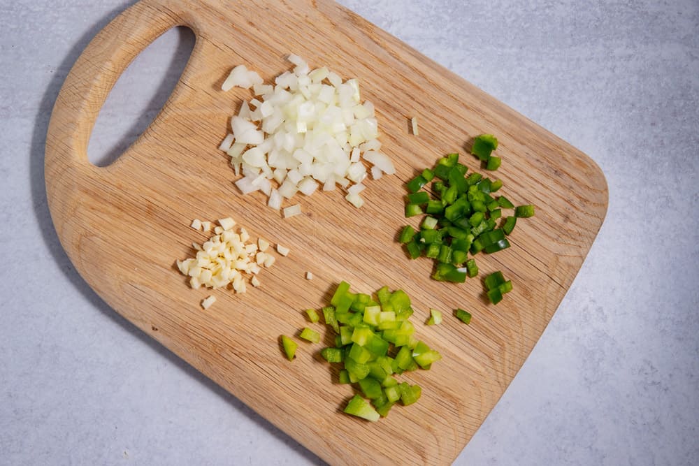 cutting board with chopped onions, jalapenos, green bell peppers, and garlic