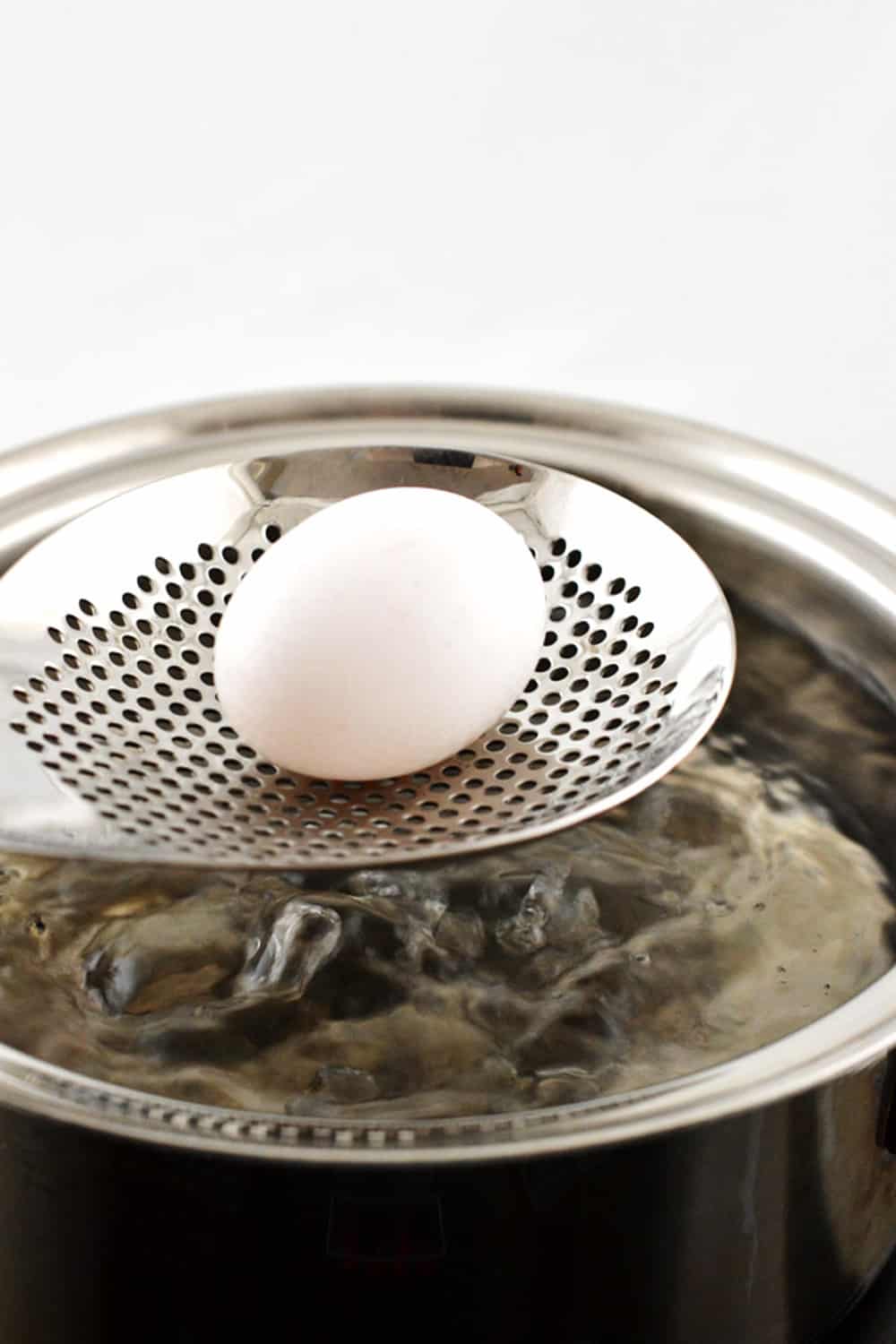 pulling egg out of boiling water with slotted spoon