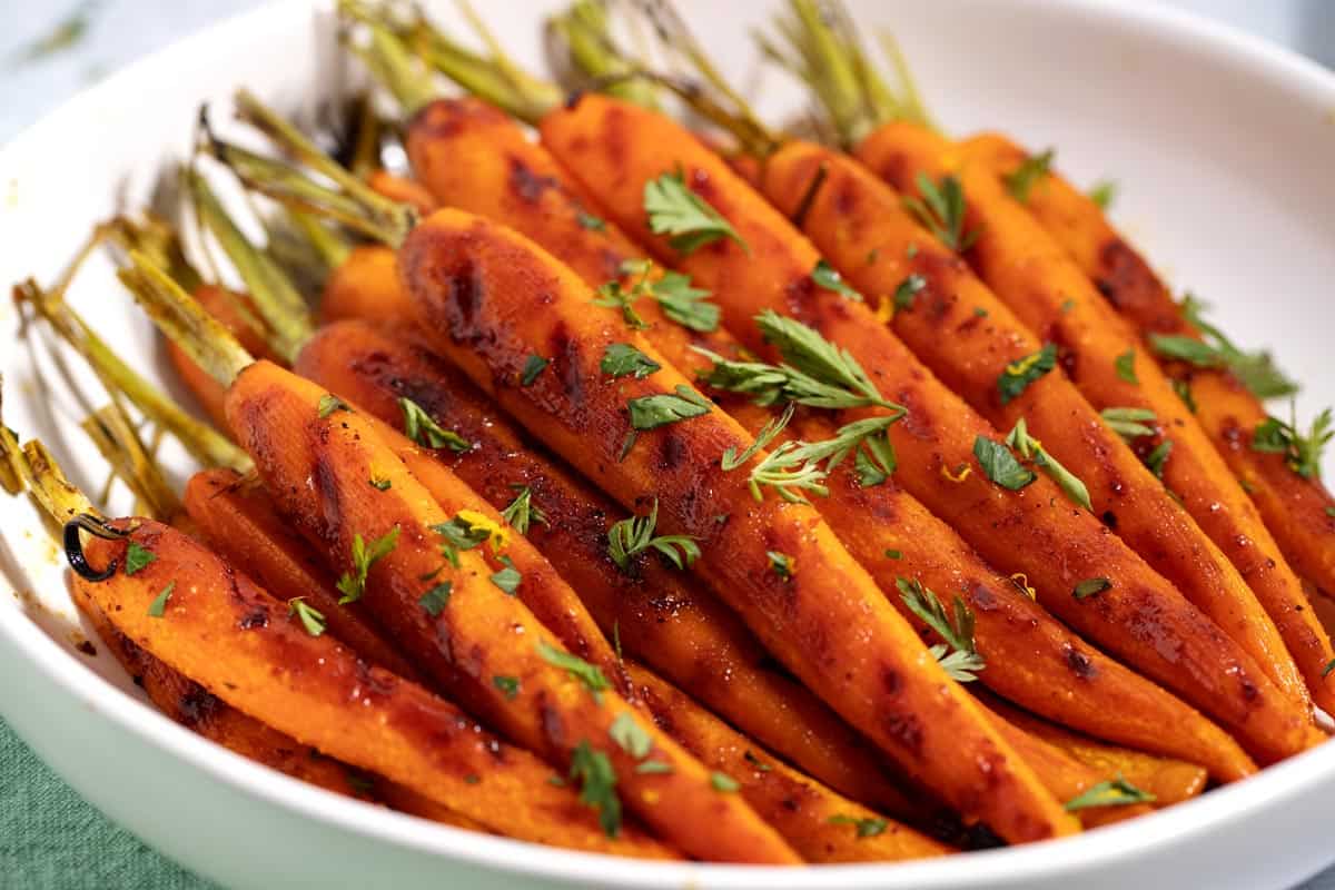 bowl of roasted carrots with glaze and carrot top garnish