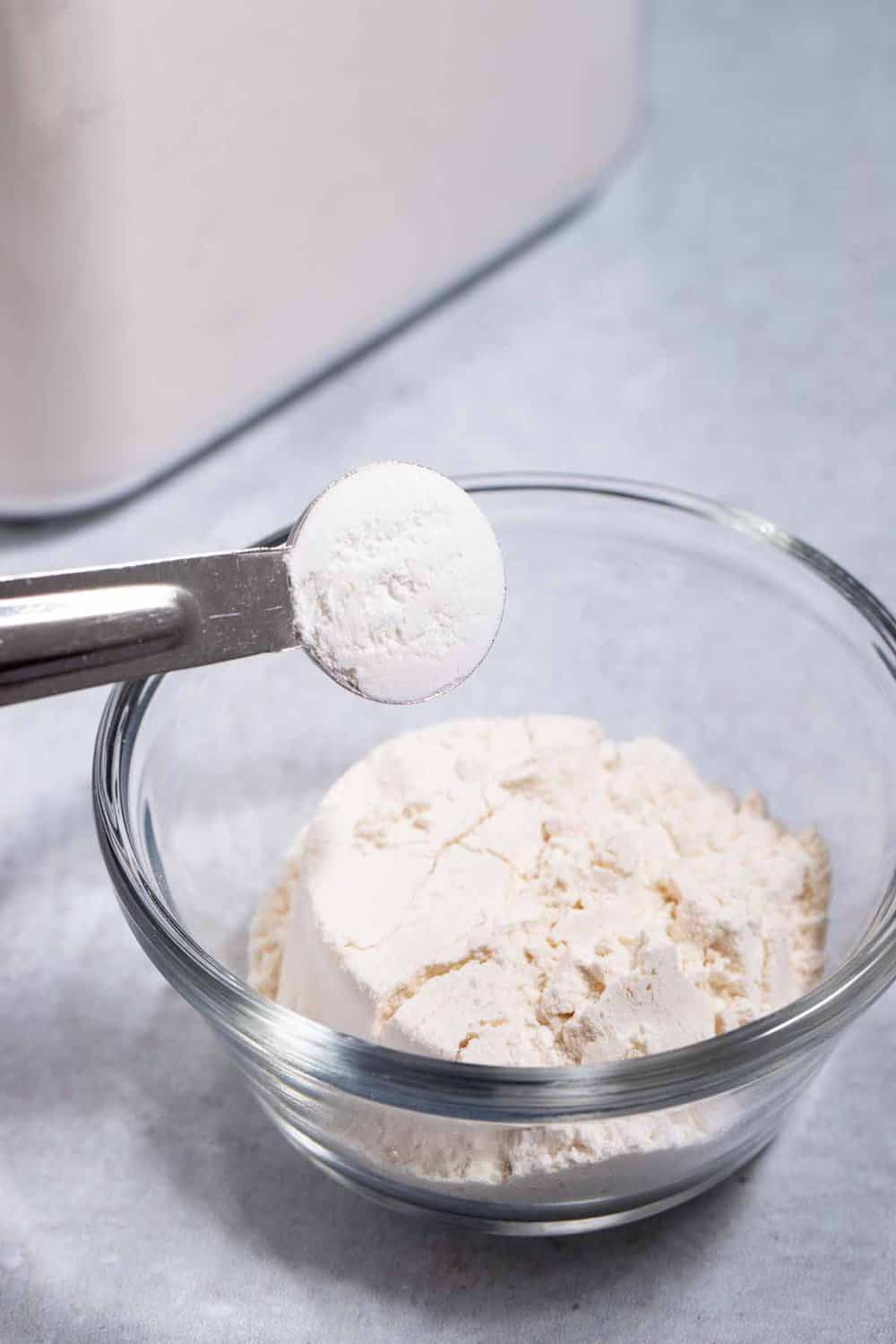 Bowl of cake mix with a teaspoon of leavener hovering over it.