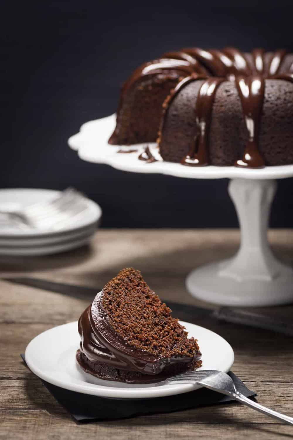 slice of chocolate cake on plate with whole cake in background