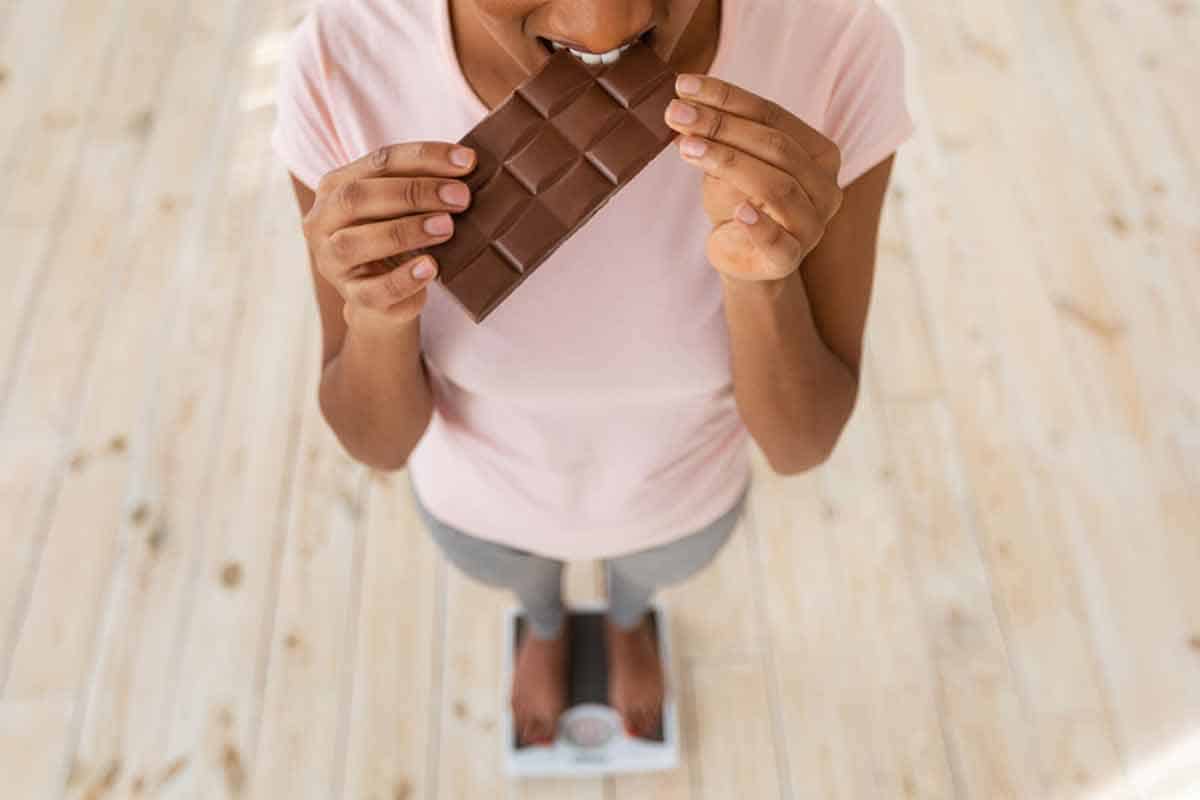 Woman eating chocolate on scale.