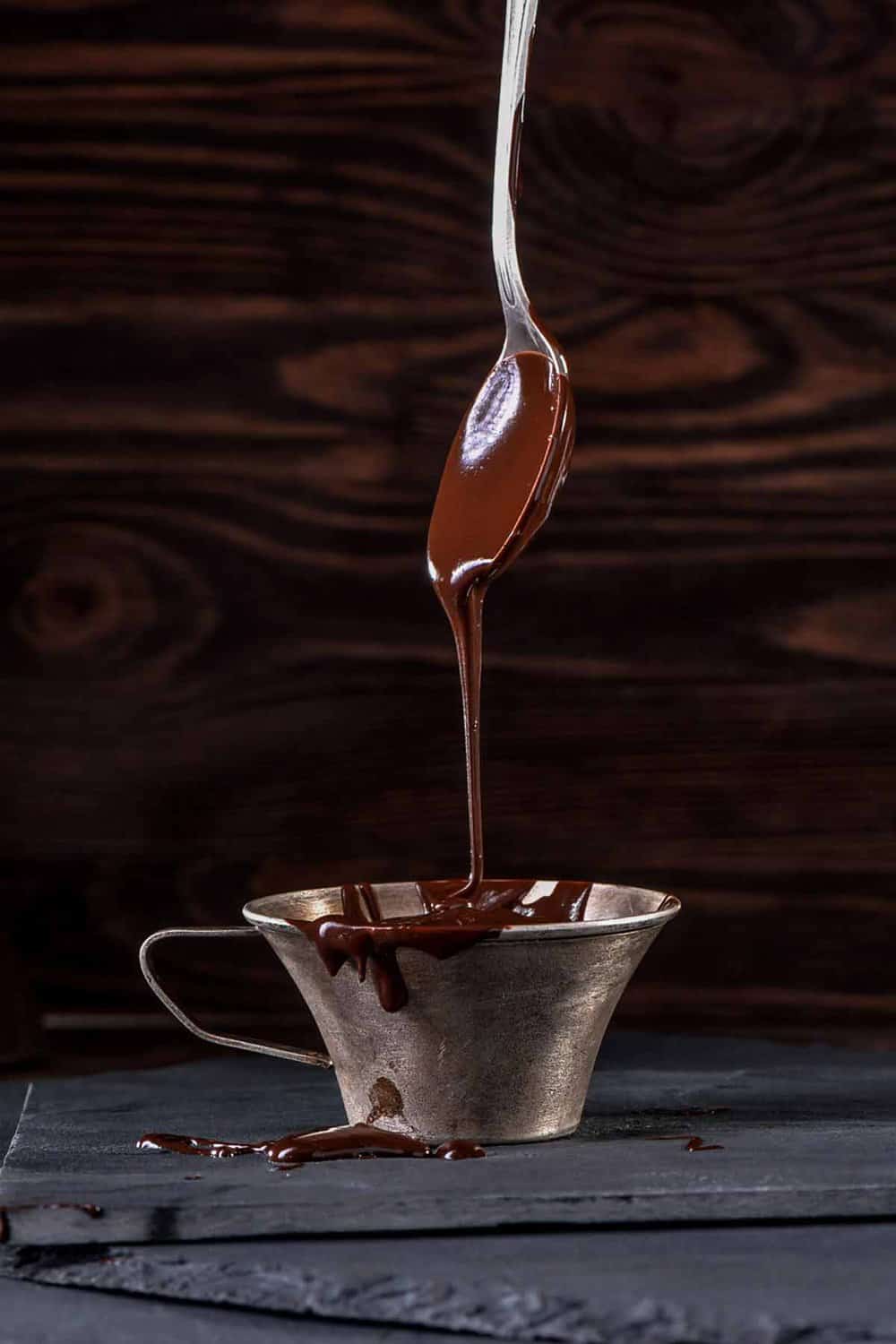 Melted milk chocolate dripping from a spoon into a cup.