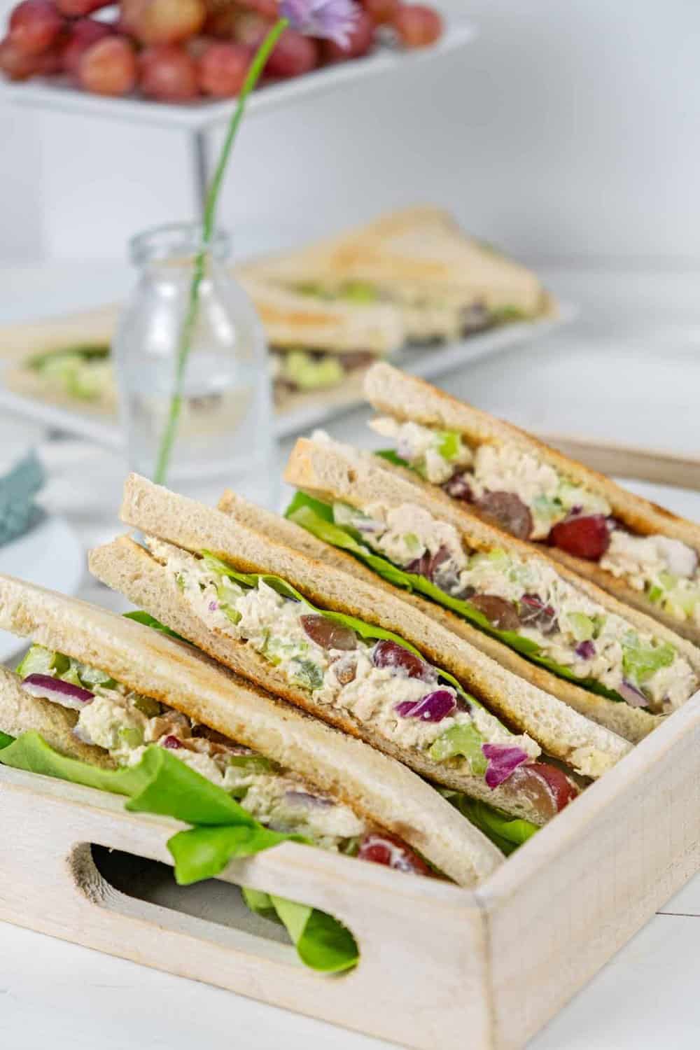 Serving container of chicken salad sandwiches with grapes.