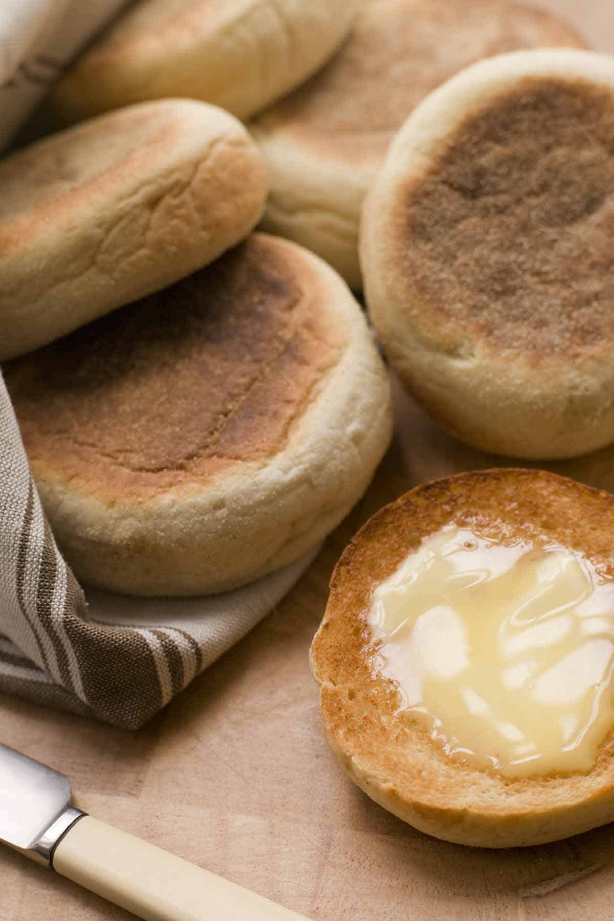 Stack of English muffins with one sliced and buttered.