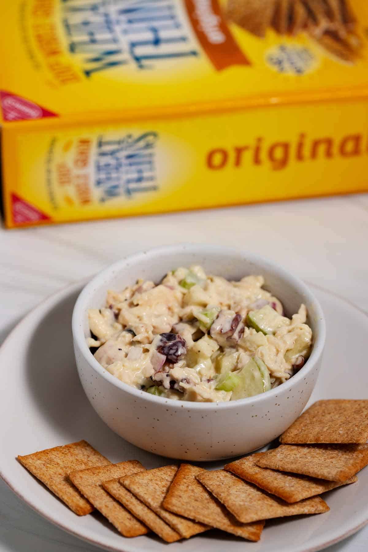 Bowl of chicken salad on a plate with crackers surrounding it.
