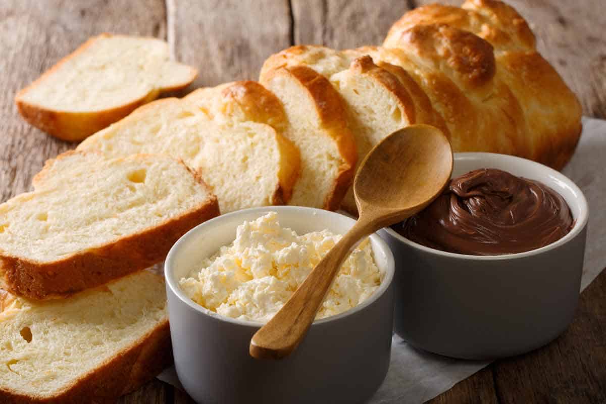Loaf of sliced brioche bread with a bowl of mascarpone and a bowl of chocolate spread.