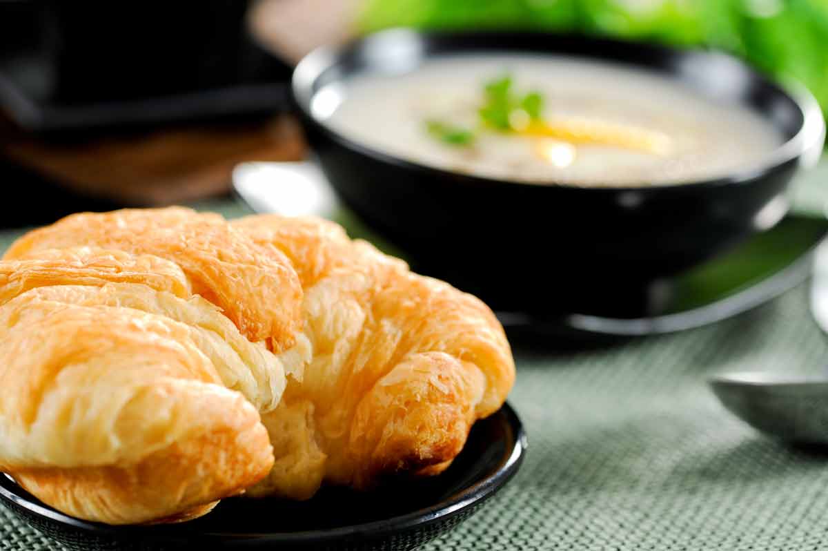 Croissant on a plate with a bowl of soup in the background.