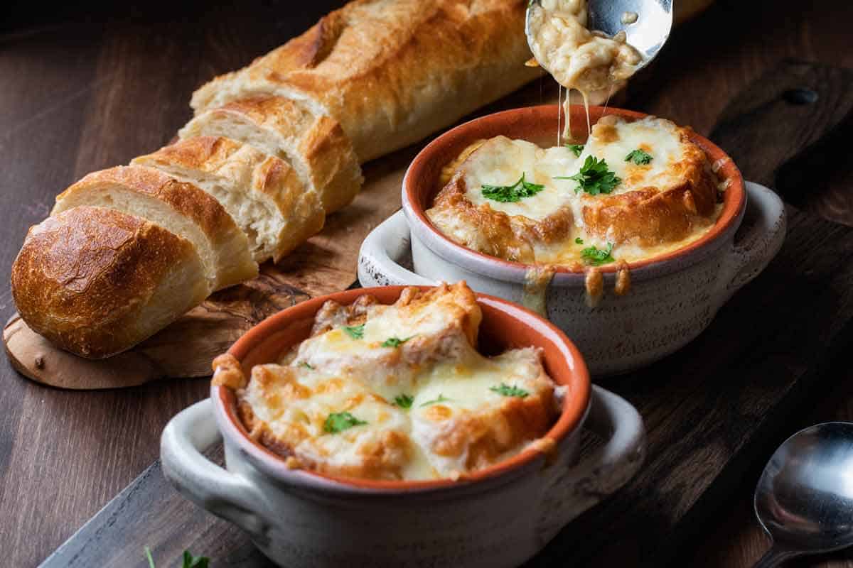 Loaf of crusty bread next to two bowls of French onion soup.