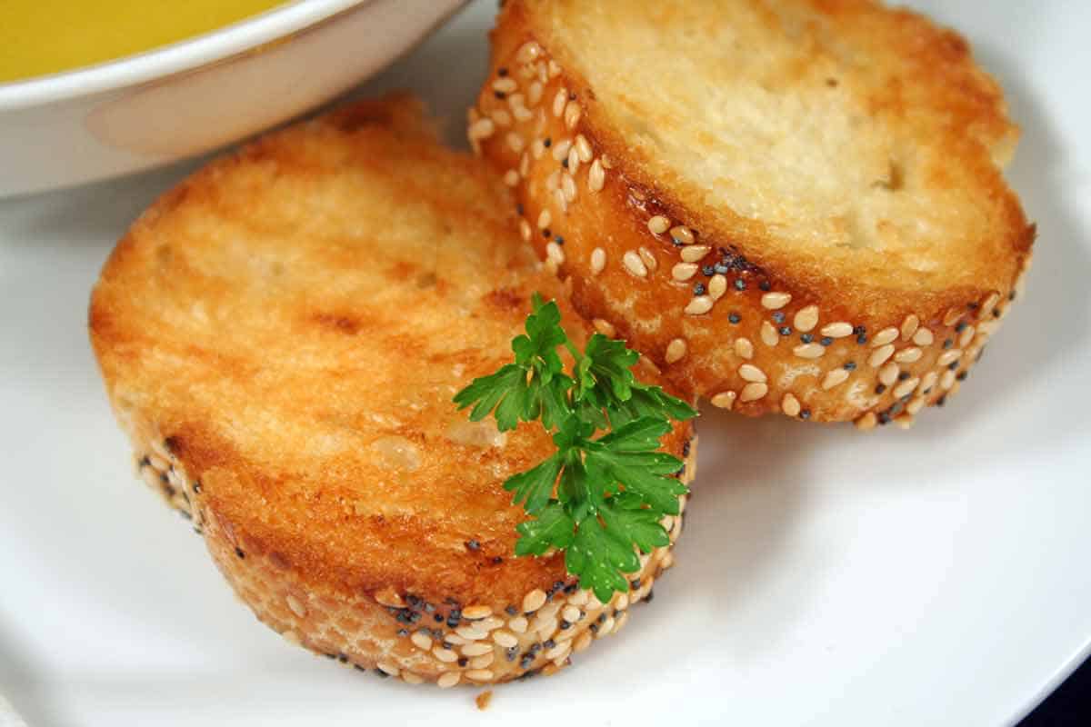 Two slices of garlic bread on a plate next to a bowl of soup.