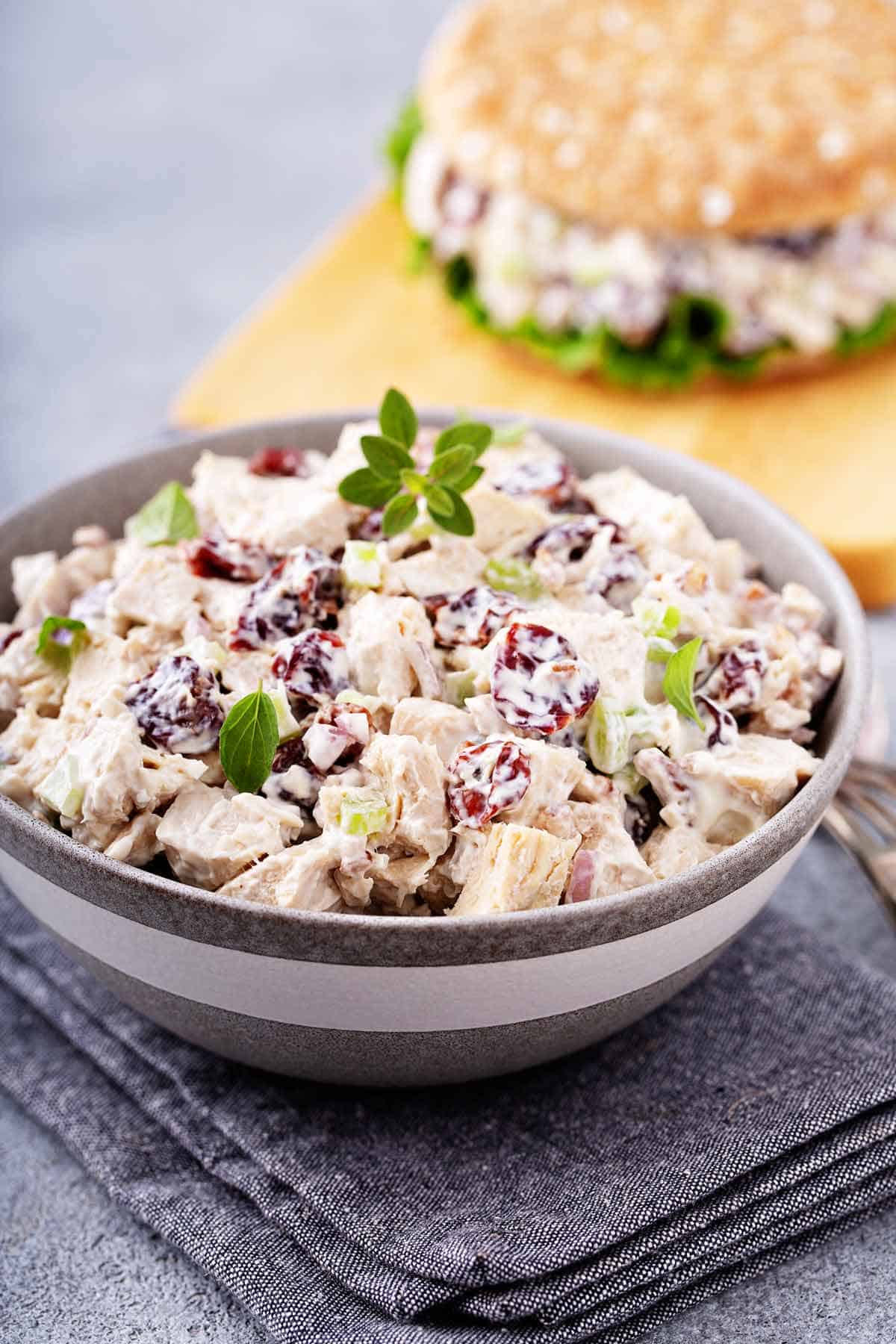 Closeup of bowl of chicken salad with chicken salad sandwich in the background.