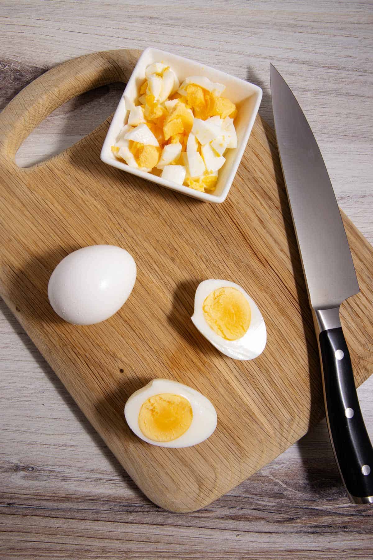 Hard-boiled eggs being chopped on a cutting board.