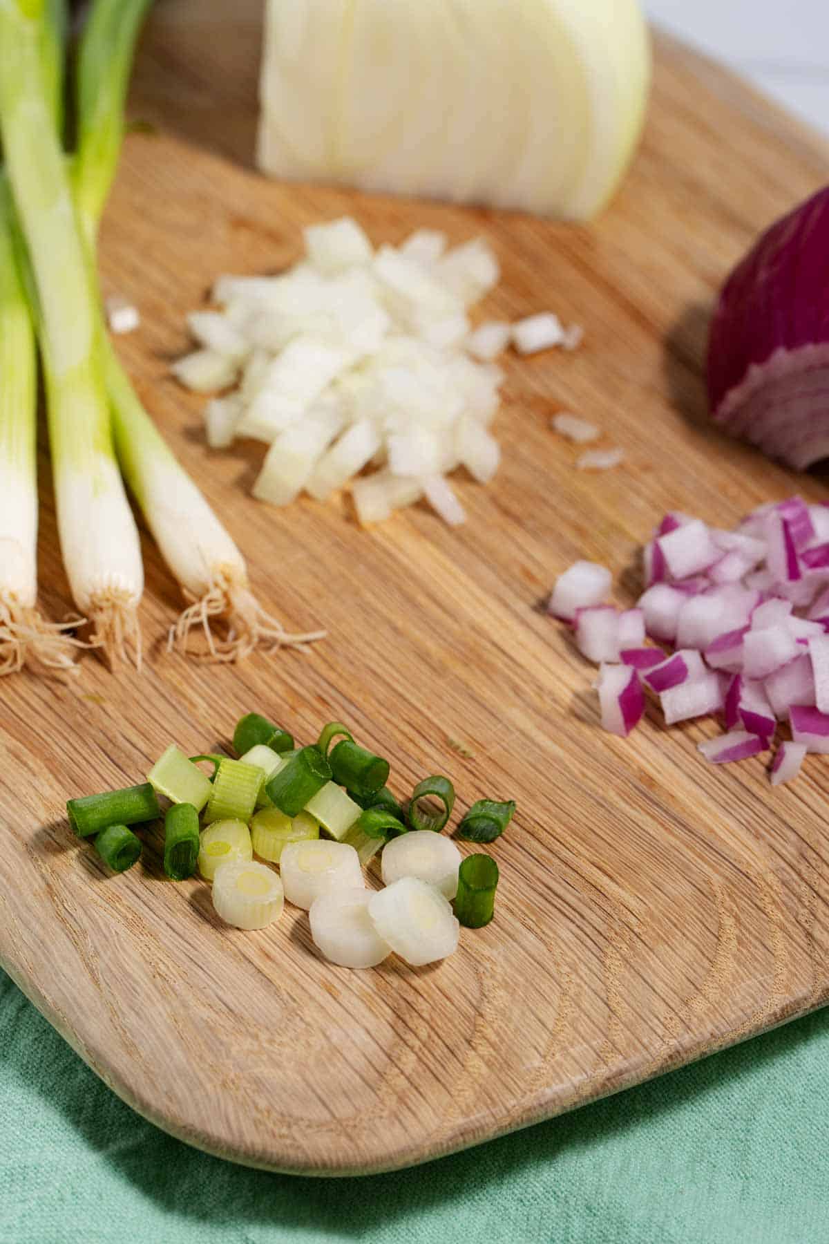 Green onions, red onions, and white onions being chopped on a cutting board.