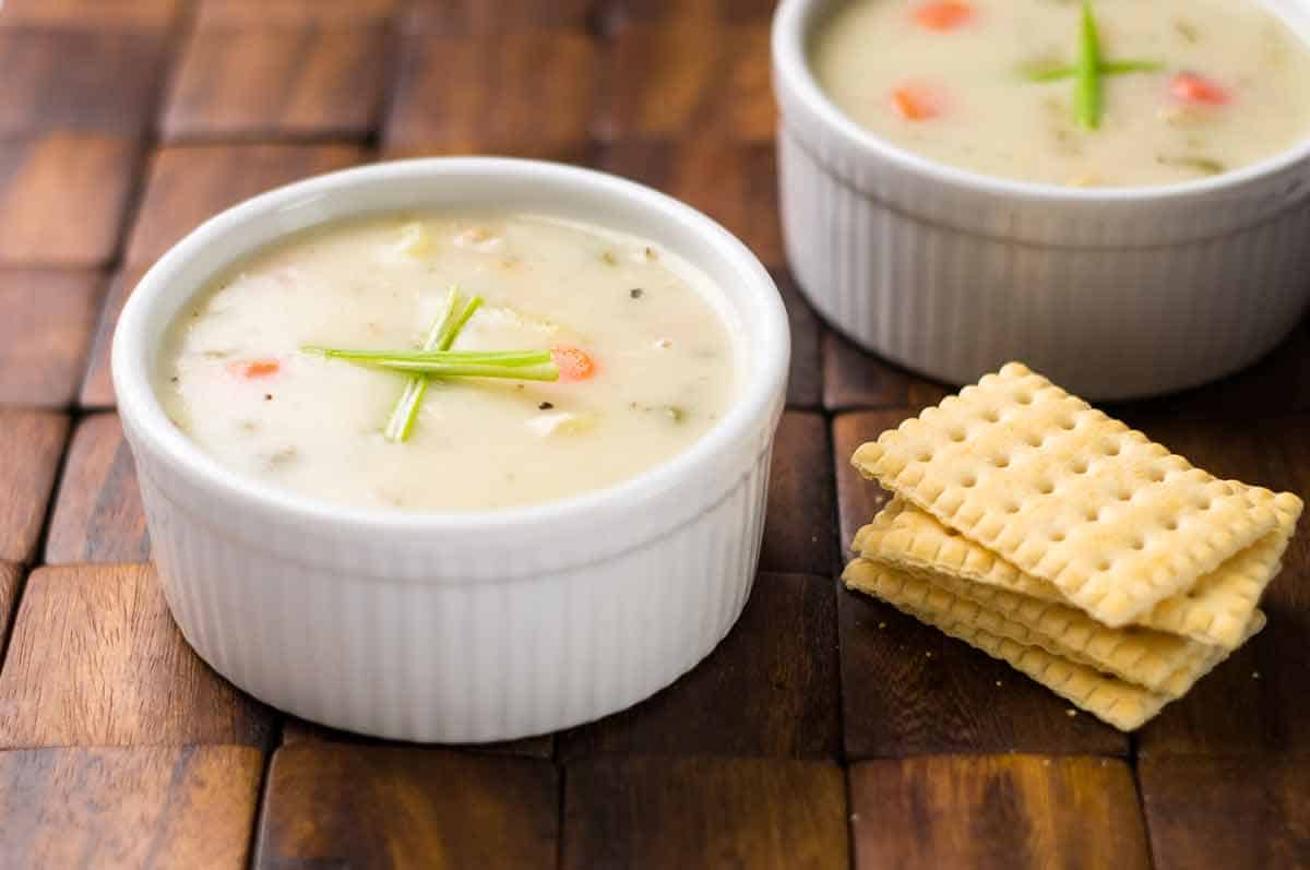 Two bowls of soup with a stack of crackers.