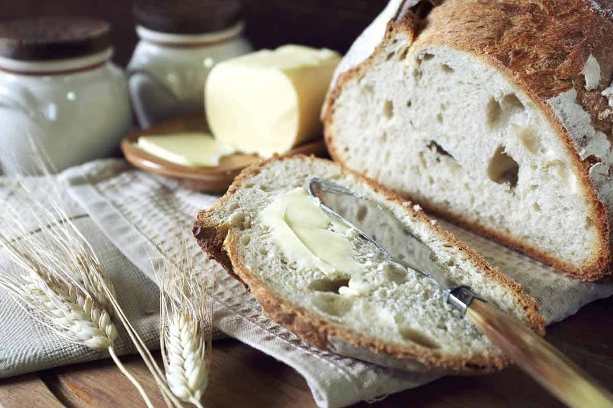 A slice of sourdough bread next to a whole loaf with a stick of butter.