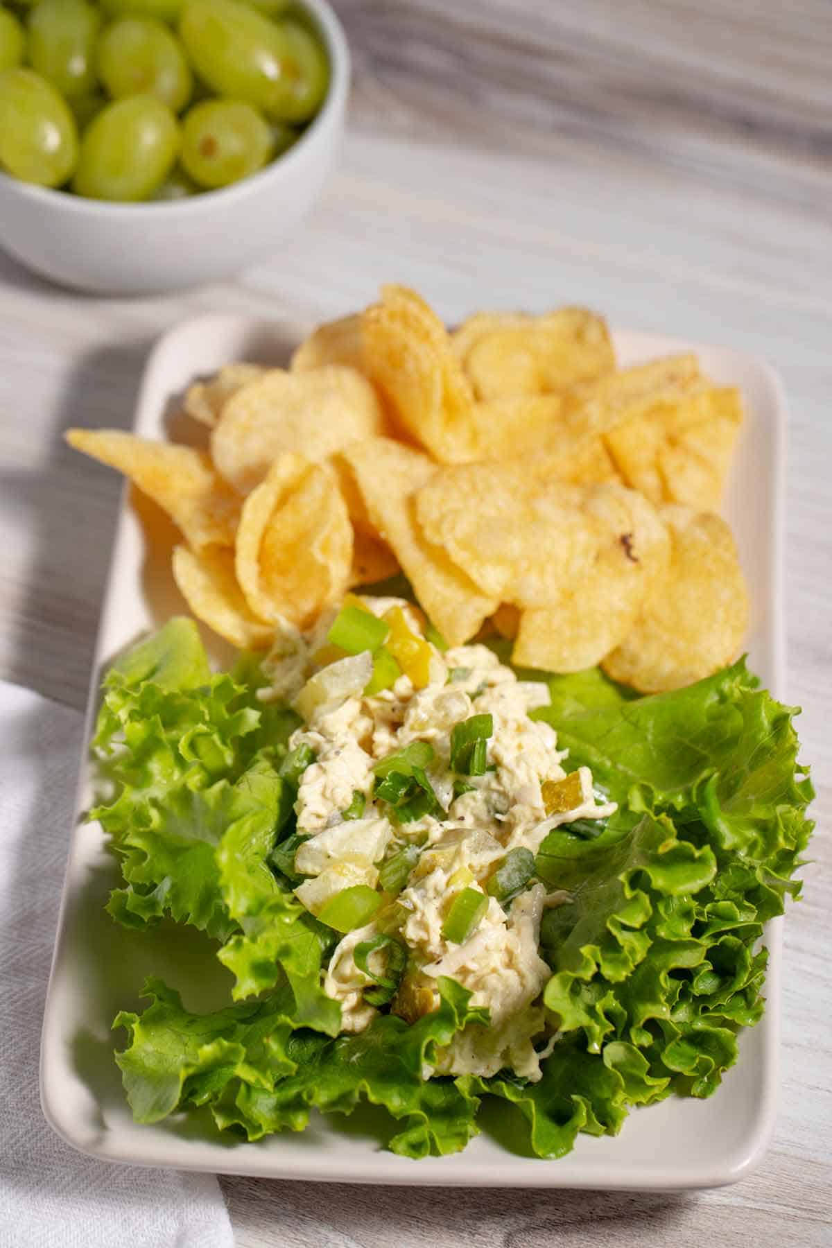 Chicken salad on a bed of greens with a side of chips and grapes.