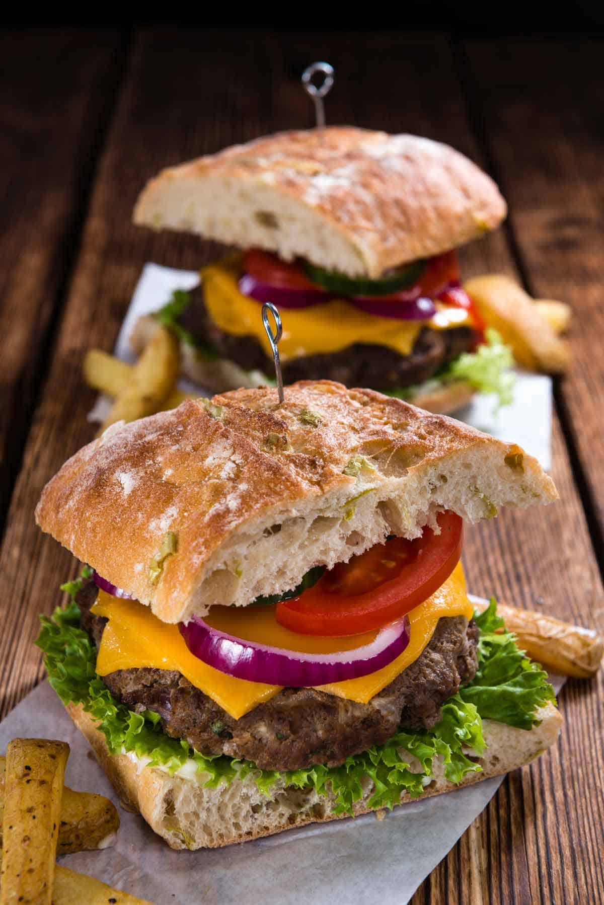 Ciabatta bread burger with lettuce, beef, cheese, red onion, and tomato.