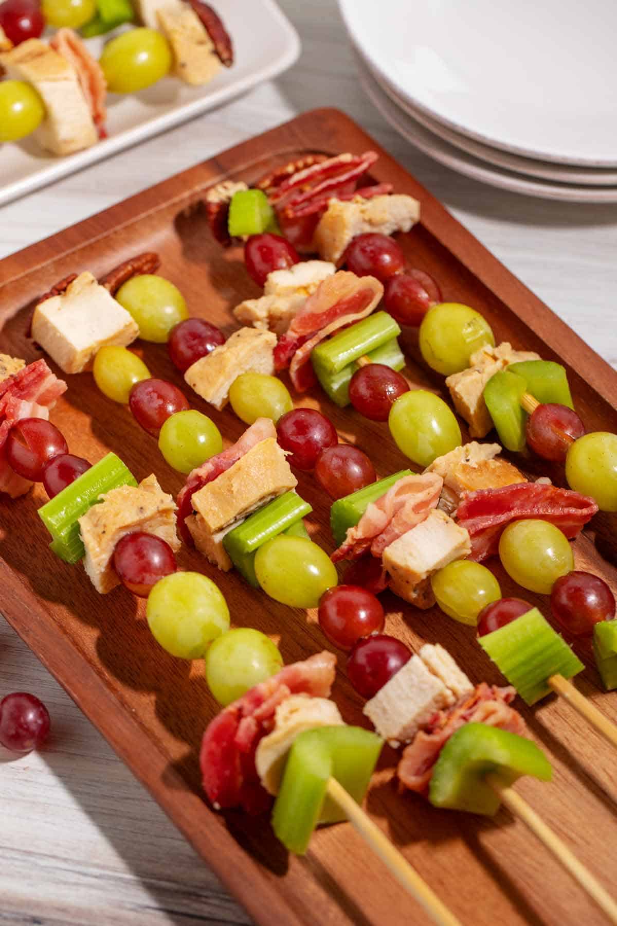 A platter of chicken salad kabobs. Items of the salad, such as celery, chicken, bacon, grapes, and a pecan are skewered.