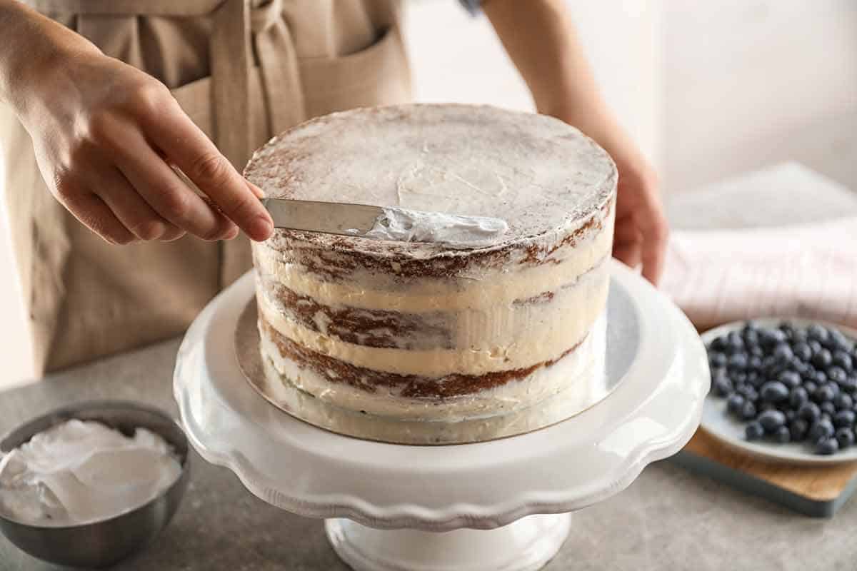 Woman smoothing a crumb coat in a layered cake.