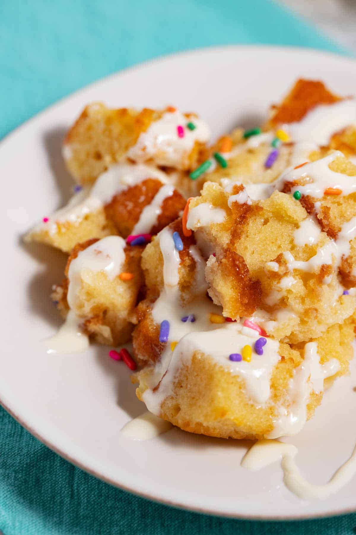 Plate of leftover cake bread pudding with vanilla sauce and sprinkles.