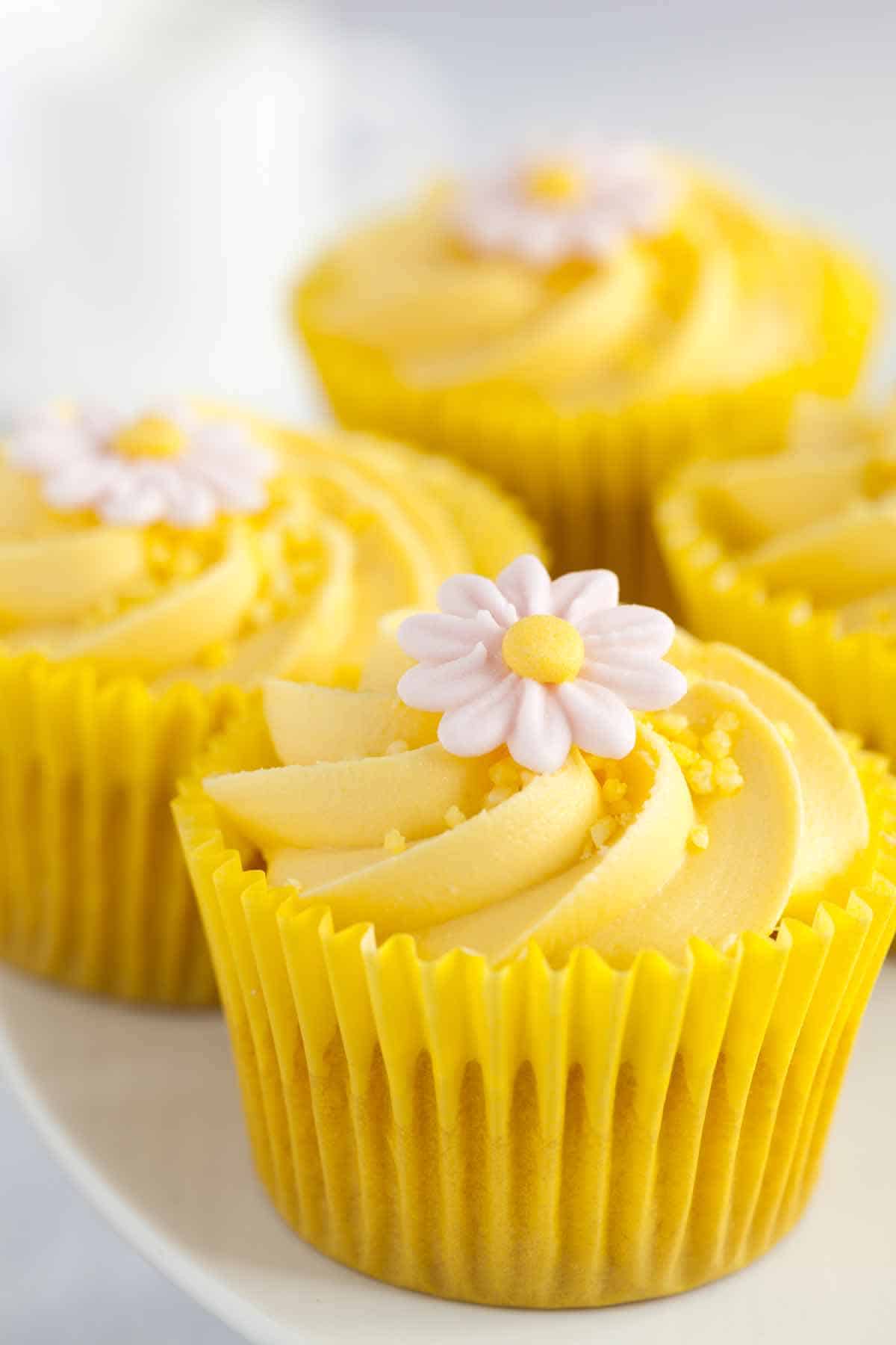 Lemon cupcakes filled and topped with lemon buttercream frosting. Each cupcake has a decorative flower on top.