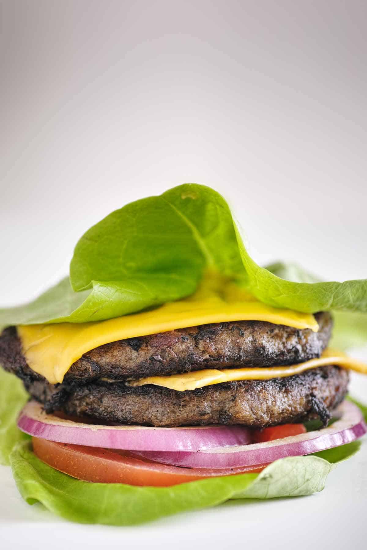 A 2-patty burger with tomato, cheese, and red onion served with a lettuce leaf bun.