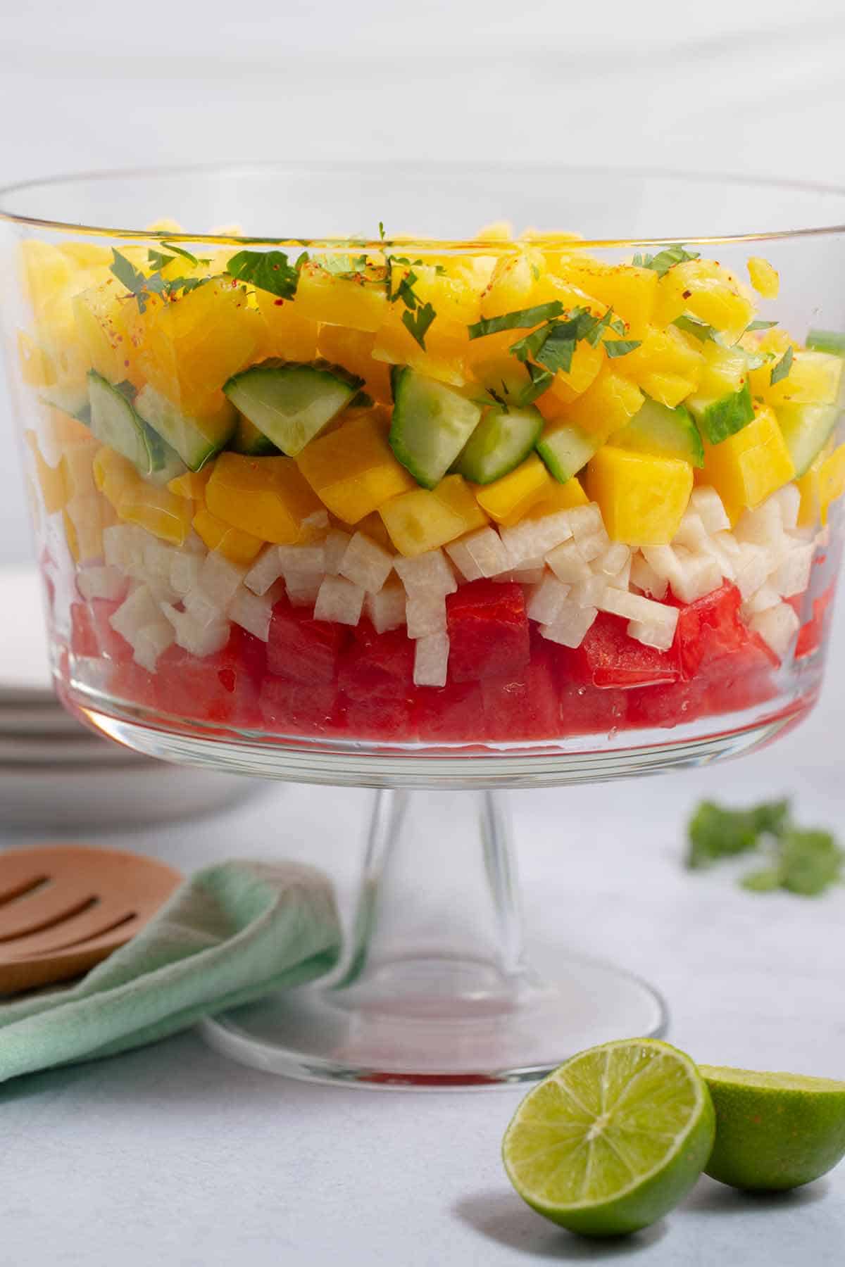 Layered ingredients of fruit salad in a glass trifle dish.